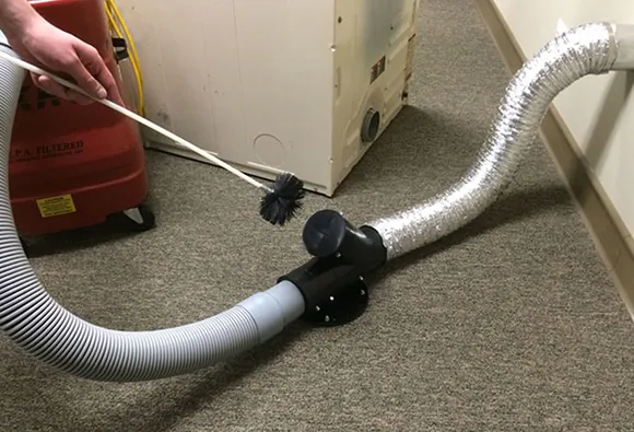 Flexible silver dryer hose connected to a dryer and an exhaust duct system in laundry.