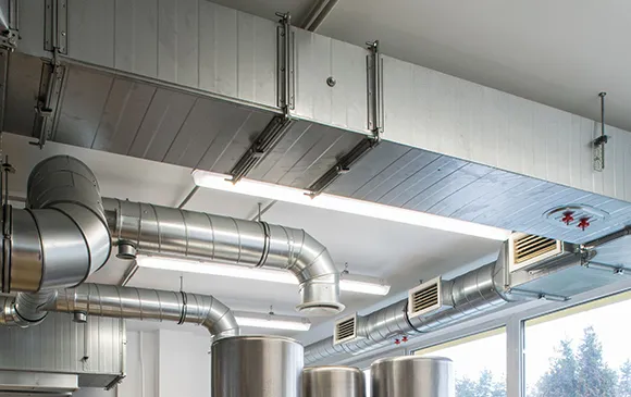 Wide shot of industrial HVAC duct system with large metal pipes in commercial building ceiling.