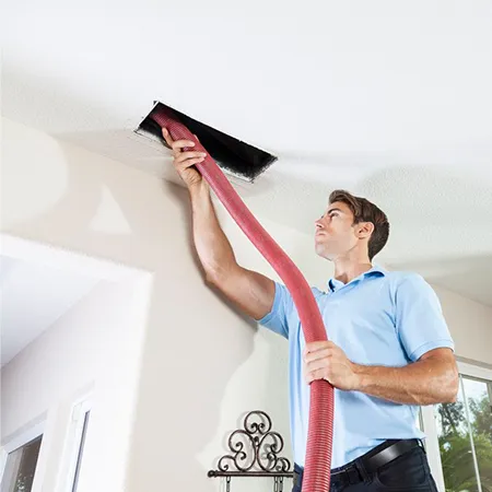 Technician using vacuum hose to clean ceiling air ducts as part of benefits of air duct cleaning services.