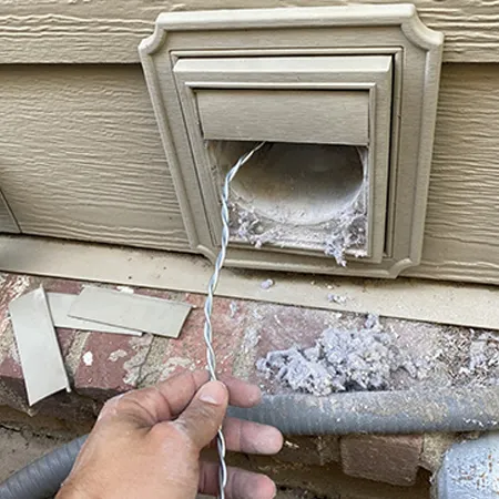 Technician removing lint and debris buildup from clogged exterior dryer vent for air duct cleaning service.