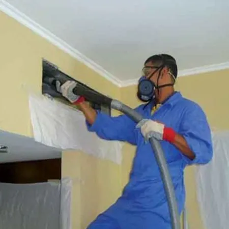 Technician in blue protective suit spraying disinfectant inside air vent during air duct cleaning in Sheboygan WI.