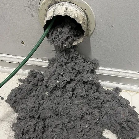 Professional technician removing heavy lint accumulation from indoor dryer vent using vacuum hose in Appleton WI.