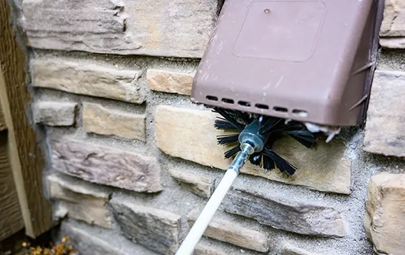 Close-up of dryer vent brush cleaning lint from exterior stone wall vent for comprehensive dryer vent cleaning and fire prevention.