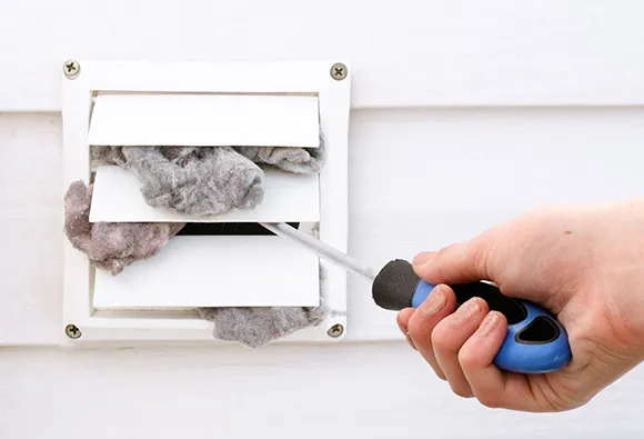 Hand cleaning clogged dryer vent outlet with specialized brush tool for improved airflow.