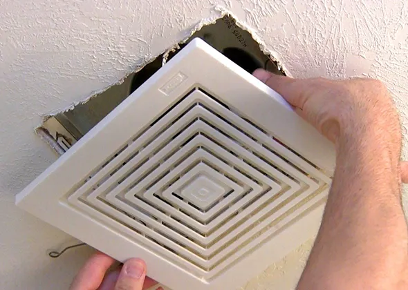 Expert bathroom fan motor cleaning with technician removing vent cover in West Bend WI bathroom.