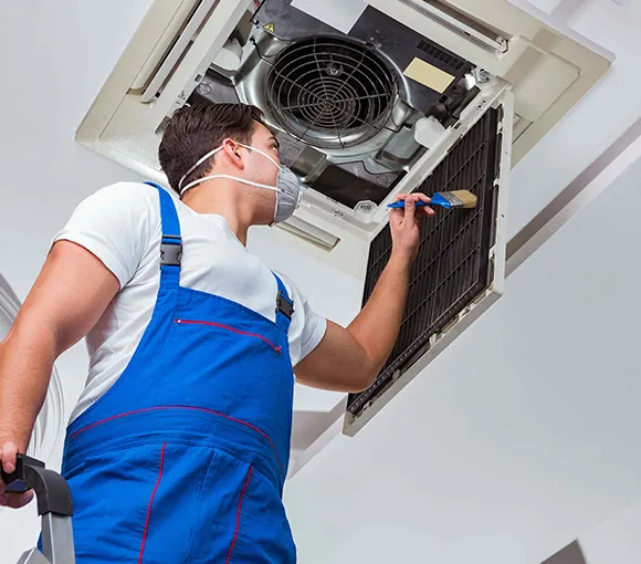 HVAC duct cleaning technician wearing blue overalls and protective mask performing duct maintenance in Green Bay WI.