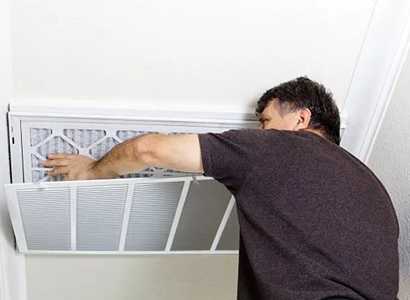 Technician inspecting residential air duct vent grille for maintenance in Madison WI.