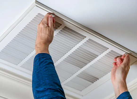 Person removing ceiling air vent cover for professional air duct cleaning.