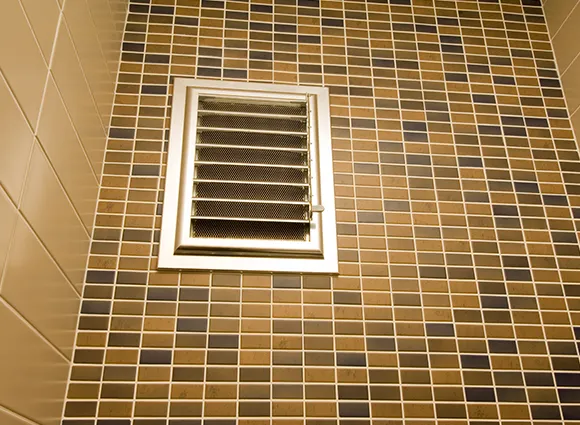 Professional vent fan dust removal with clean brown tiled wall and white vent grill in Green Bay WI bathroom.