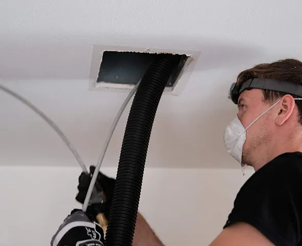Air duct cleaning technician wearing protective mask using specialized equipment to clean duct system in Sheboygan WI home.