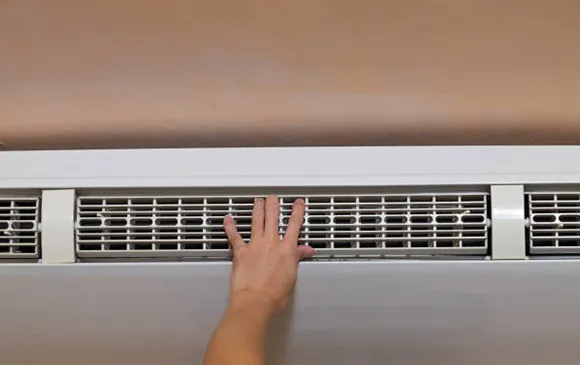 Close-up of hand adjusting a white HVAC air vent grille in indoor wall.