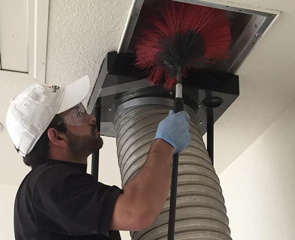 Technician wearing cap cleaning mold-contaminated flexible air duct with specialized brush in Green Bay WI home.