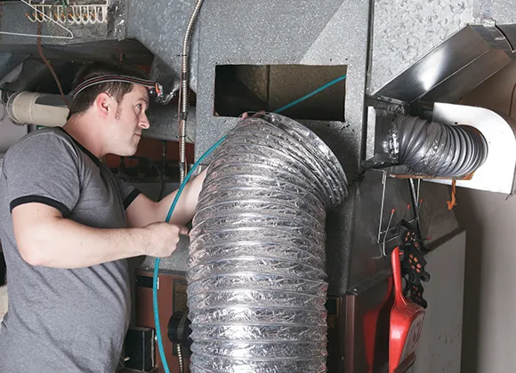 Reliable commercial air duct cleaning experts using hose to clean duct system in West Bend WI.