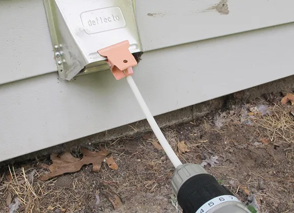 Technician cleaning external dryer vent with specialized brush tool for dryer vent maintenance.