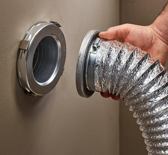 Technician connecting or inspecting flexible dryer vent hose attached to dryer outlet in Janesville WI home.
