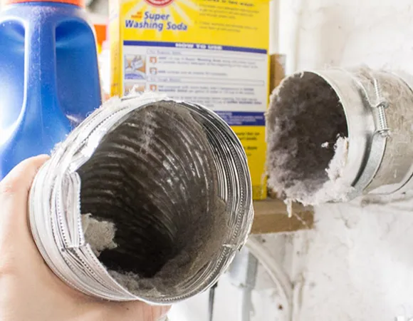 Set of flexible silver dryer vent hoses installed near laundry detergent bottles in laundry room.