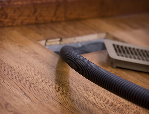 Vacuum hose cleaning air vent on hardwood floor during residential air duct sanitization in Oshkosh WI.