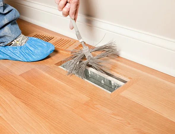 Professional cleaning and disinfecting air vent on hardwood floor for thorough air vent cleaning in Marinette WI.