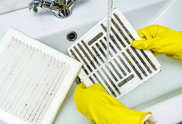 Thorough bathroom fan cleaning service with gloved hands scrubbing exhaust fan grille in West Bend WI.