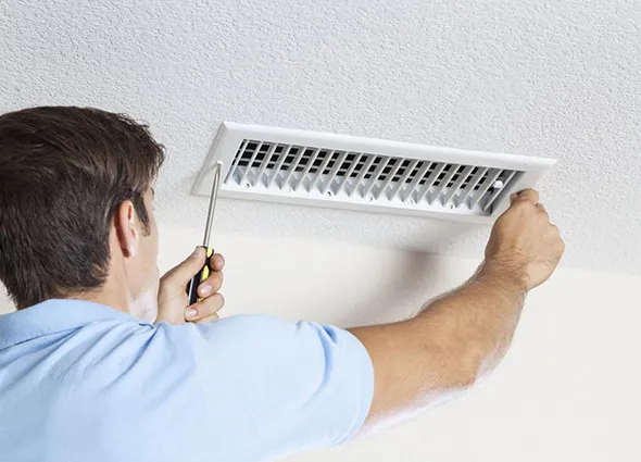 HVAC technician inspecting and cleaning wall-mounted air vent in Appleton WI home