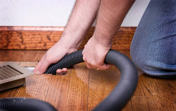 Professional air duct cleaning using vacuum equipment on hardwood floor in Manitowoc WI.