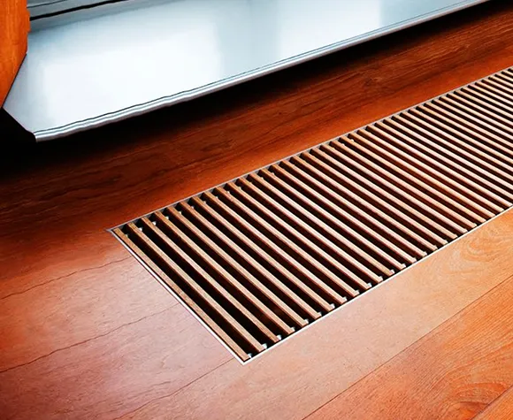 Close-up of a floor air vent grille on polished wooden flooring for trusted air duct cleaning services.