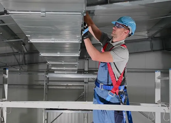HVAC technician inspecting and cleaning commercial duct system in industrial or commercial building.