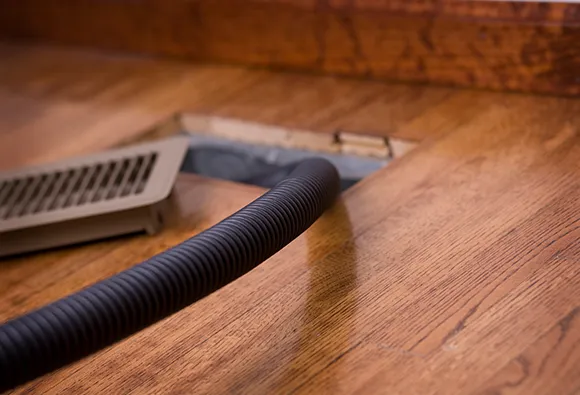 Trusted air duct cleaning company using vacuum hose to clean floor air vent in West Bend WI.